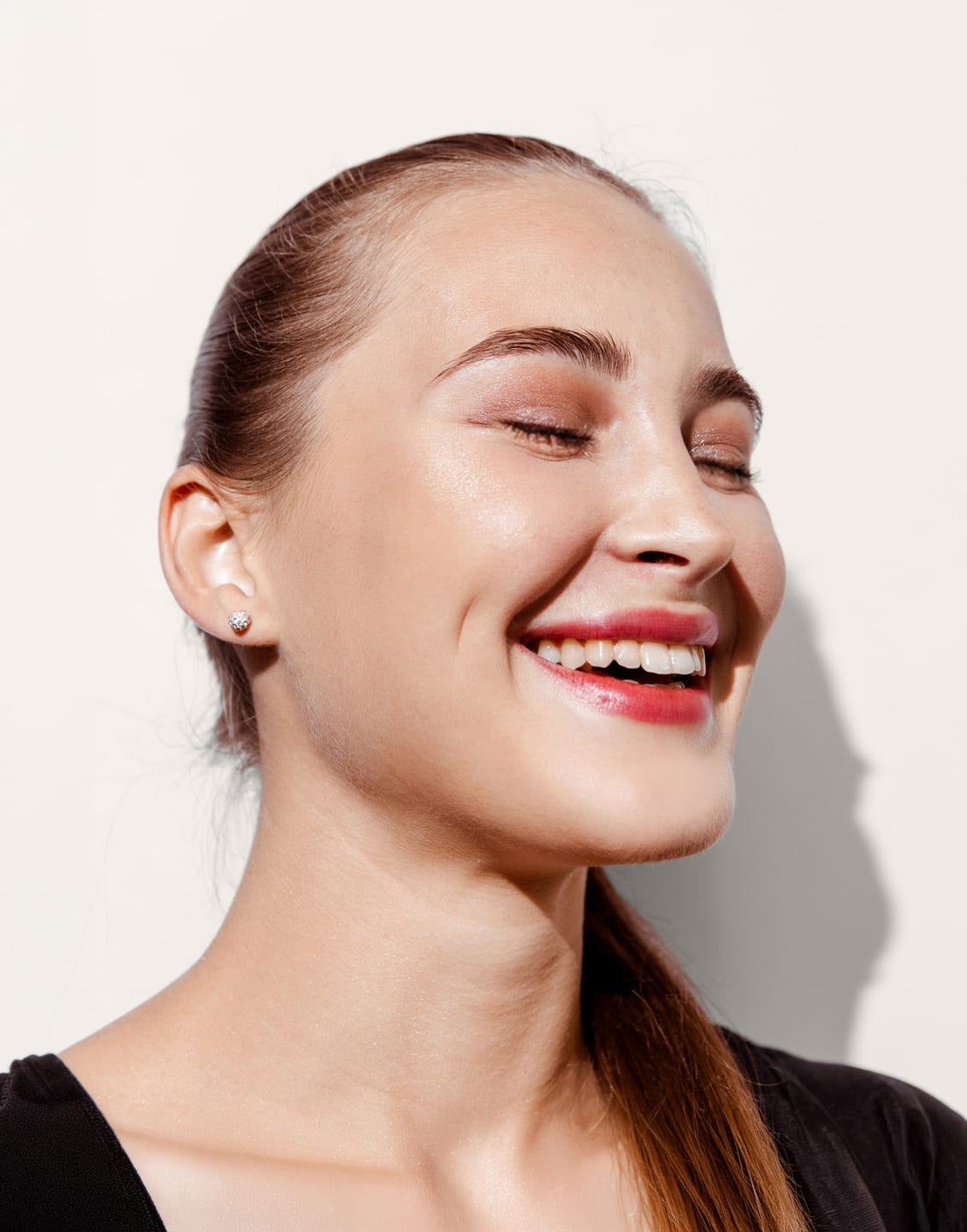 Woman laughing with her eyes closed and hair tied back