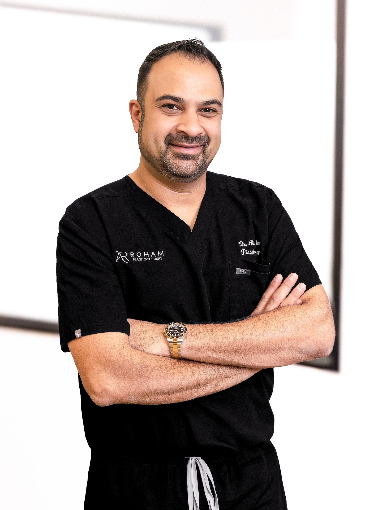 Dr. Ali Roham standing with his arms crossed in black Roham Plastic Surgery scrubs