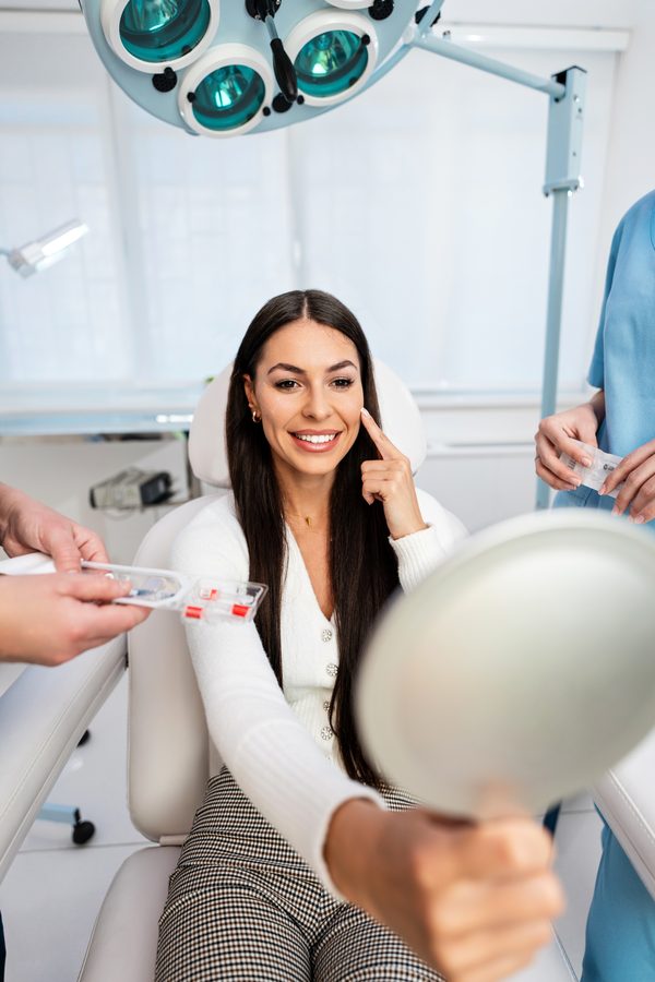 Smiling patient in a treatment chair holding a hand mirror to review her results