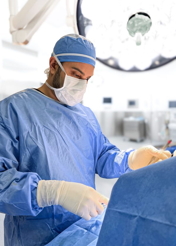 Surgeon in blue scrubs and mask operating under theatre lights